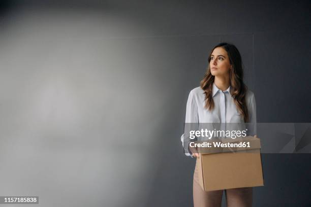 serious young businesswoman holding cardboard box - downsizing unemployment stock-fotos und bilder