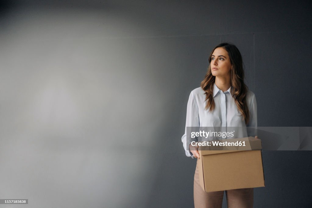 Serious young businesswoman holding cardboard box