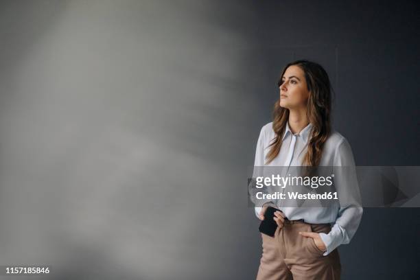 portrait of serious young businesswoman with cell phone looking sideways - sideways glance stock pictures, royalty-free photos & images