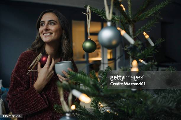 smiling young woman decorating christmas tree - advent stock-fotos und bilder