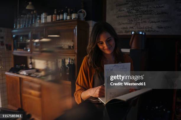 smiling young woman looking into guestbook at restaurant counter - gastenboek stockfoto's en -beelden