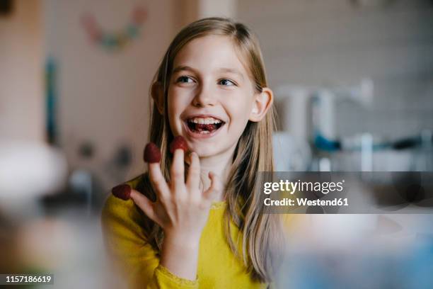 happy girl sitting at kitchen table at home playing with raspberries - player portraits stock-fotos und bilder