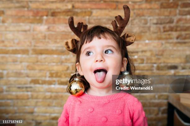 portrait of toddler girl sticking out tongue wearing reindeer antlers headband and christmas baubles - portrait grimace photos et images de collection