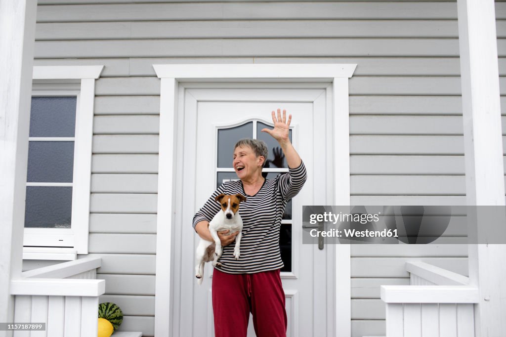 Happy senior woman on porch with her dog raising her hand