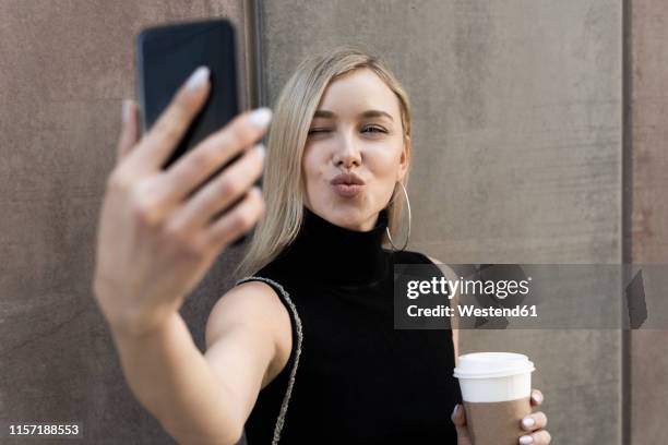 portrait of blond woman with coffee to go taking selfie with smartphone - blonde woman selfie foto e immagini stock