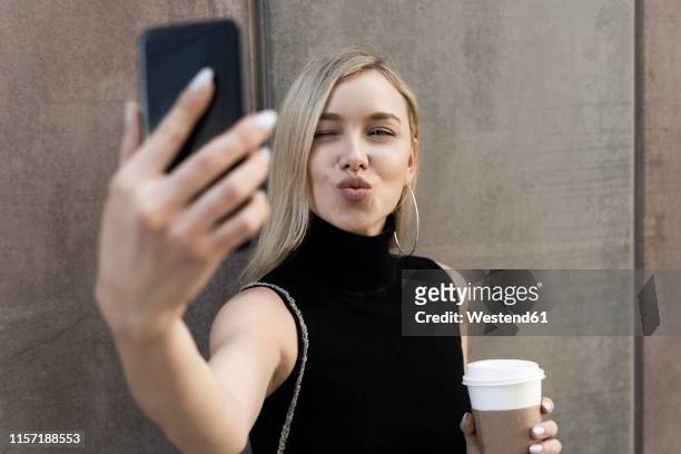 portrait of blond woman with coffee to go taking selfie with smartphone - puckering stock pictures, royalty-free photos & images