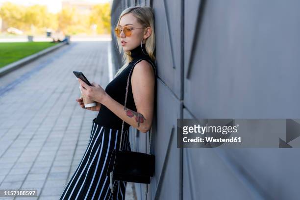 fashionable young woman leaning against wall looking at smartphone - culottes stock pictures, royalty-free photos & images
