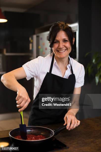 portrait of smiling woman cooking in kitchen using a pan - placa de fogão vitrocerâmica imagens e fotografias de stock