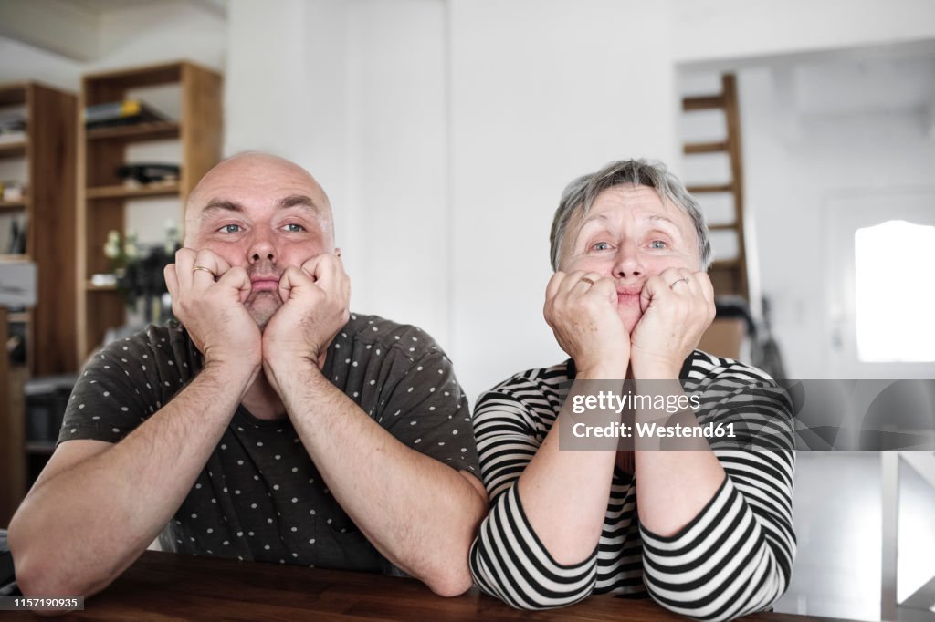 Portrait of adult son with senior mother sitting at table at home with head in hands