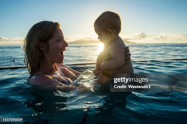 french polynesia, tahiti, papeete, woman playing with her little baby in an infinity pool at sunset - één ouder stockfoto's en -beelden