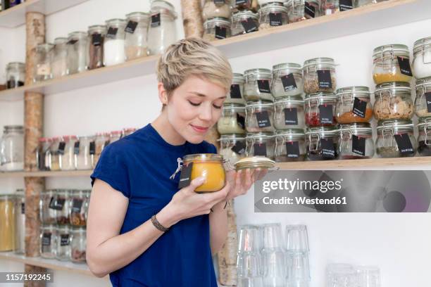 woman smelling at jar in front of spice shelf in kitchen - jars kitchen stock pictures, royalty-free photos & images