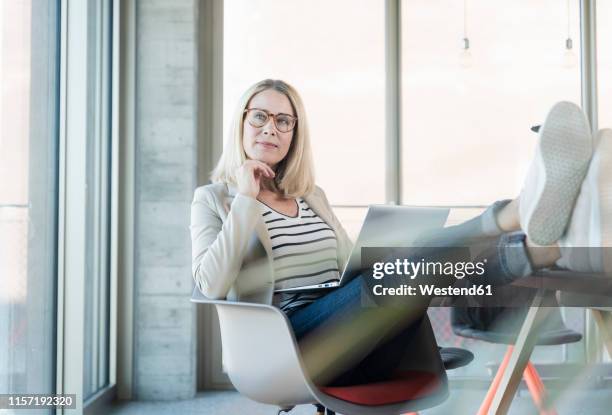 relaxed businesswoman using laptop in office with feet up - tisch betrachten stock-fotos und bilder