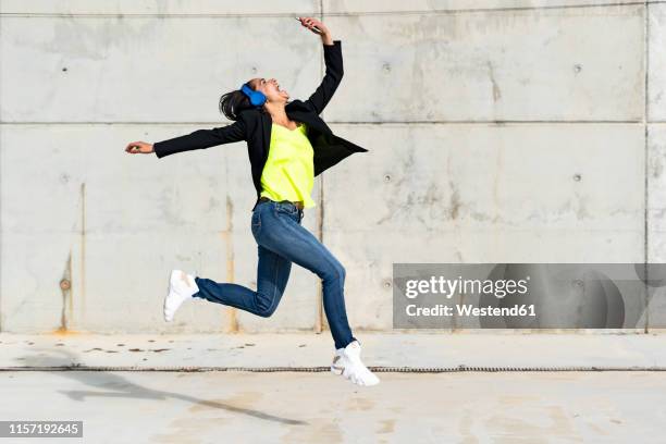 woman with blue headphones listening music, jumping in the air and taking a selfie - jumping for joy stockfoto's en -beelden