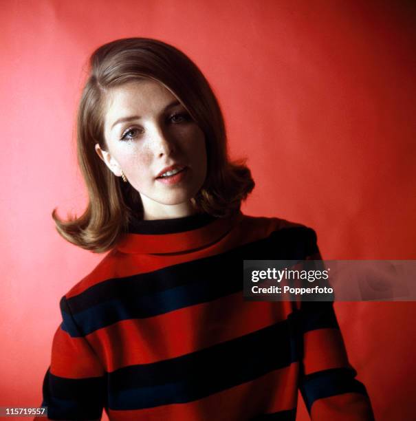 Young female model with brown medium-length hair, wearing a cowl-neck navy blue and red striped knitted top in a studio setting, circa 1965. .