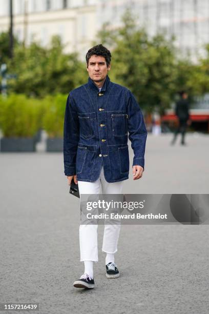 Guest wears a navy blue denim jacket, white ripped hem crop pants, black sneakers, outside Undercover, during Paris Fashion Week - Menswear...