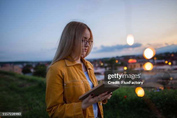 nettes mädchen liest ein buch am rande der stadt im sonnenuntergang - brille frühling stock-fotos und bilder