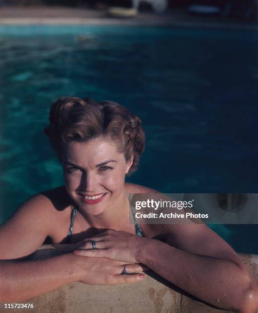 Esther Williams, US swimmer and actress, smiling as she poses in a swimming pool, her arms resting on the edge of the pool, circa 1950.