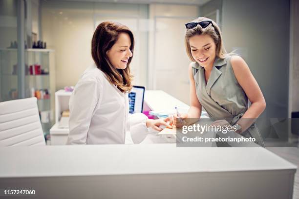 la giovane donna sta compilando documenti sulla reception della clinica di trattamento di bellezza - chirurgia estetica donna foto e immagini stock