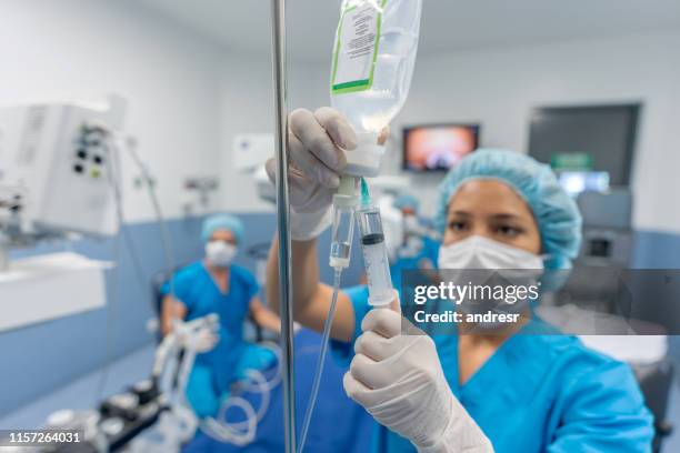 medico in sala operatoria che mette i farmaci attraverso un iv - operating room foto e immagini stock