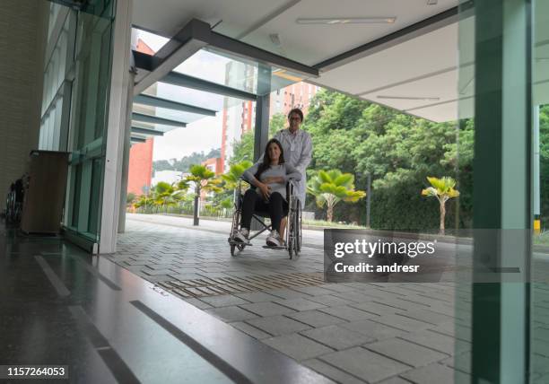 schwangere frau kommt mit einem rollstuhl ins krankenhaus - krankenhaus eingang stock-fotos und bilder