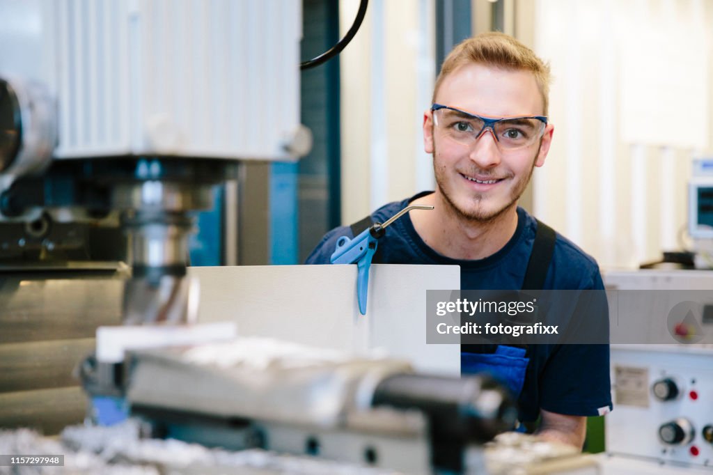 Porträt: Junger Techniker mit Schutzbrille arbeitet an einer Fräsmaschine