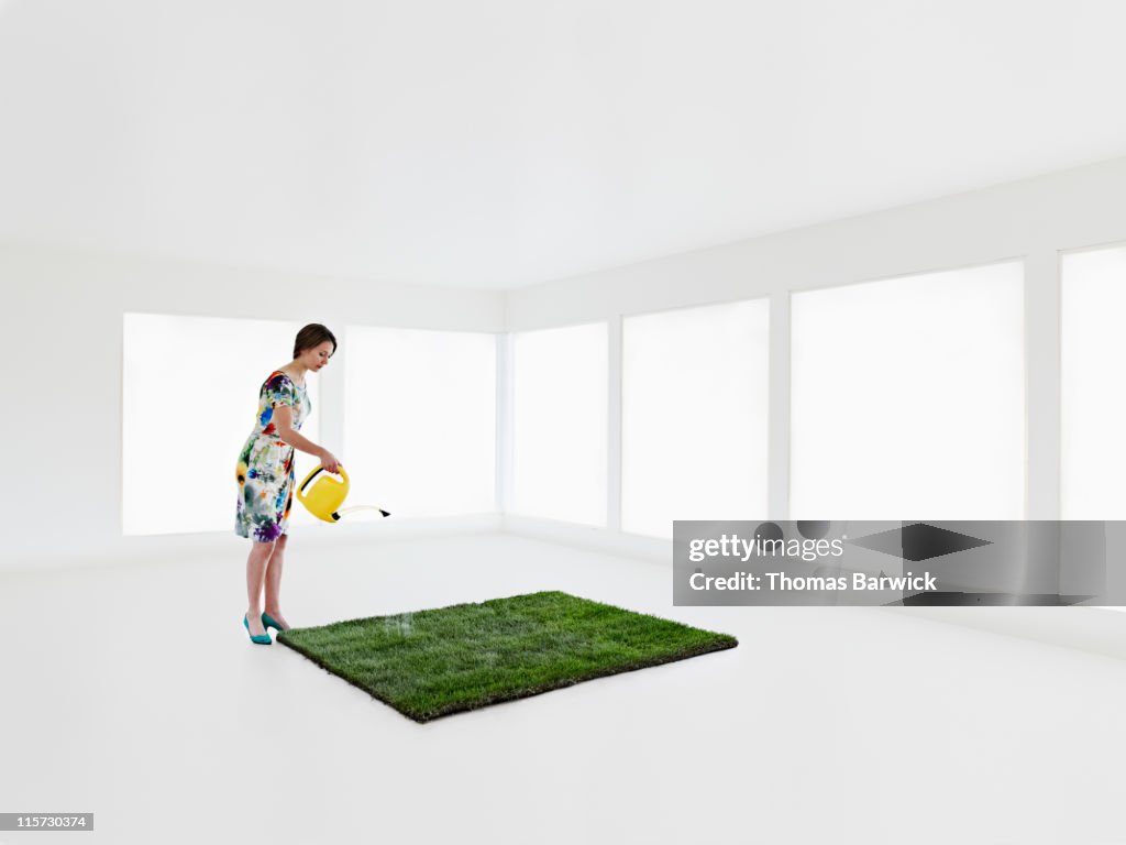 Woman watering patch of grass in empty home