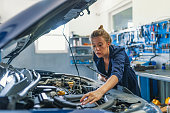 Lovely female auto mechanic, examining engine of an automobile