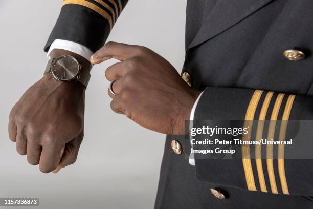 england, uk, airline pilot checking time on his wristwatch. - pilot jacket stock-fotos und bilder