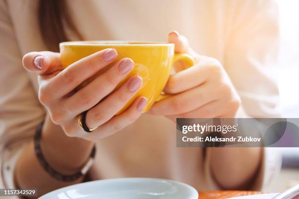 yellow mug in the hands of a young woman. girl holding a cup of coffee in a cafe. coffee break, breakfast. the concept of power. close up. - mug of tea stock pictures, royalty-free photos & images