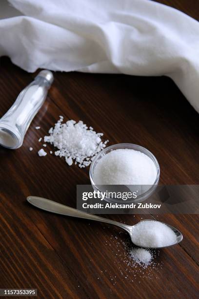 natural seasoning, organic, sea, small and large, white salt in a spoon, in a cup, in a salt shaker, poured on a wooden table. next to a linen towel. the concept of cooking healthy food, cosmetology. - zout smaakstof stockfoto's en -beelden