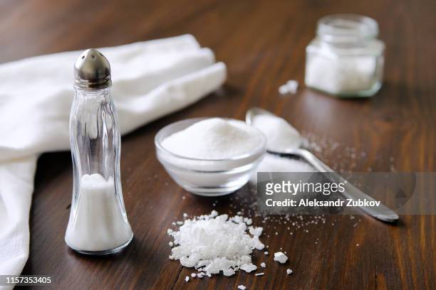 natural seasoning, organic, sea, small and large, white salt in a spoon, in a cup, in a salt shaker, poured on a wooden table. next to a linen towel. the concept of cooking healthy food, cosmetology. - zout smaakstof stockfoto's en -beelden