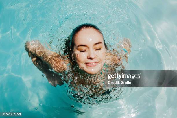 smiling young woman coming up from being submersed underwater - emerging stock-fotos und bilder