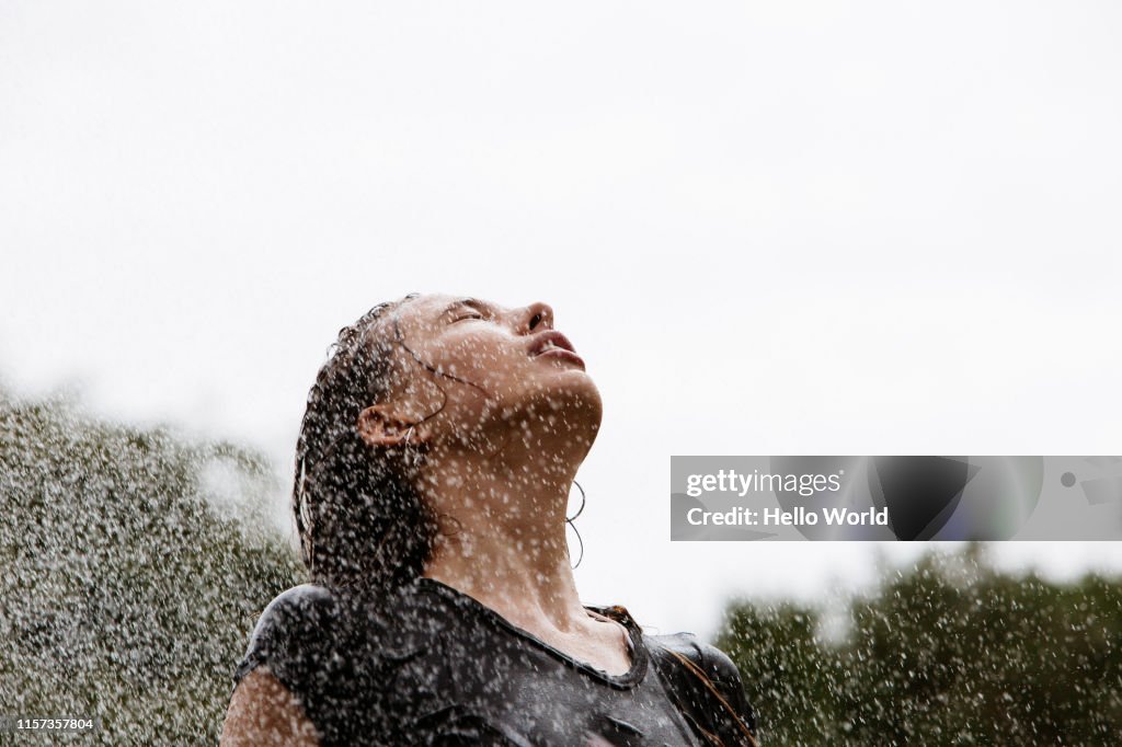Beautiful young woman enjoying sprinkler spray on face