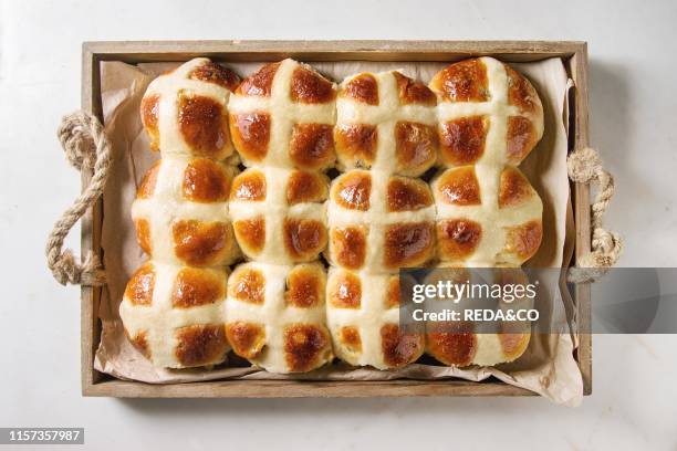 Homemade Easter traditional hot cross buns in wooden tray tray with baking paper over white marble background. Top view. Space.