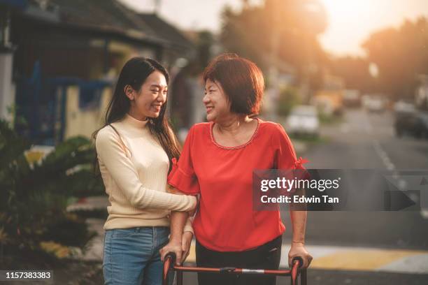 an asian chinese female walking with her walking aid recovering and helped by her daughter - mature woman and son imagens e fotografias de stock