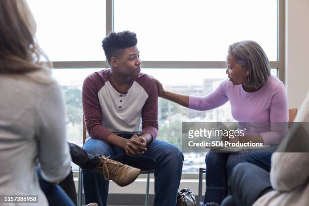mature grandmother lays hand on teen grandson to reassure him - emotional support stock pictures, royalty-free photos & images
