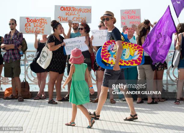 Tourists walk by protesters that demonstrate against the shooting of Woody Allen's new film in the Spanish Basque city of San Sebastian on July 23,...