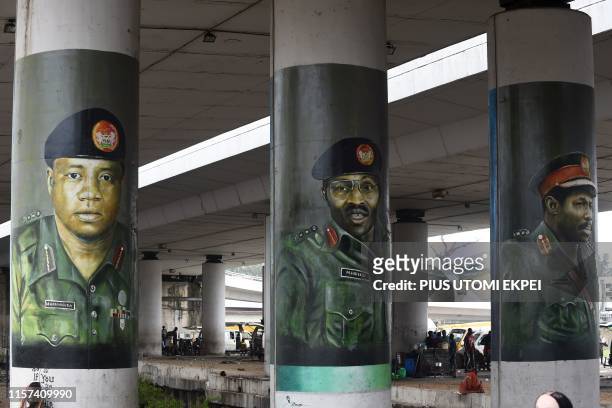 People stand under the bridge at Obalende in Lagos, on July 23, 2019 by pillars with street art portraits of President Mohammadu Buhari , flanked by...