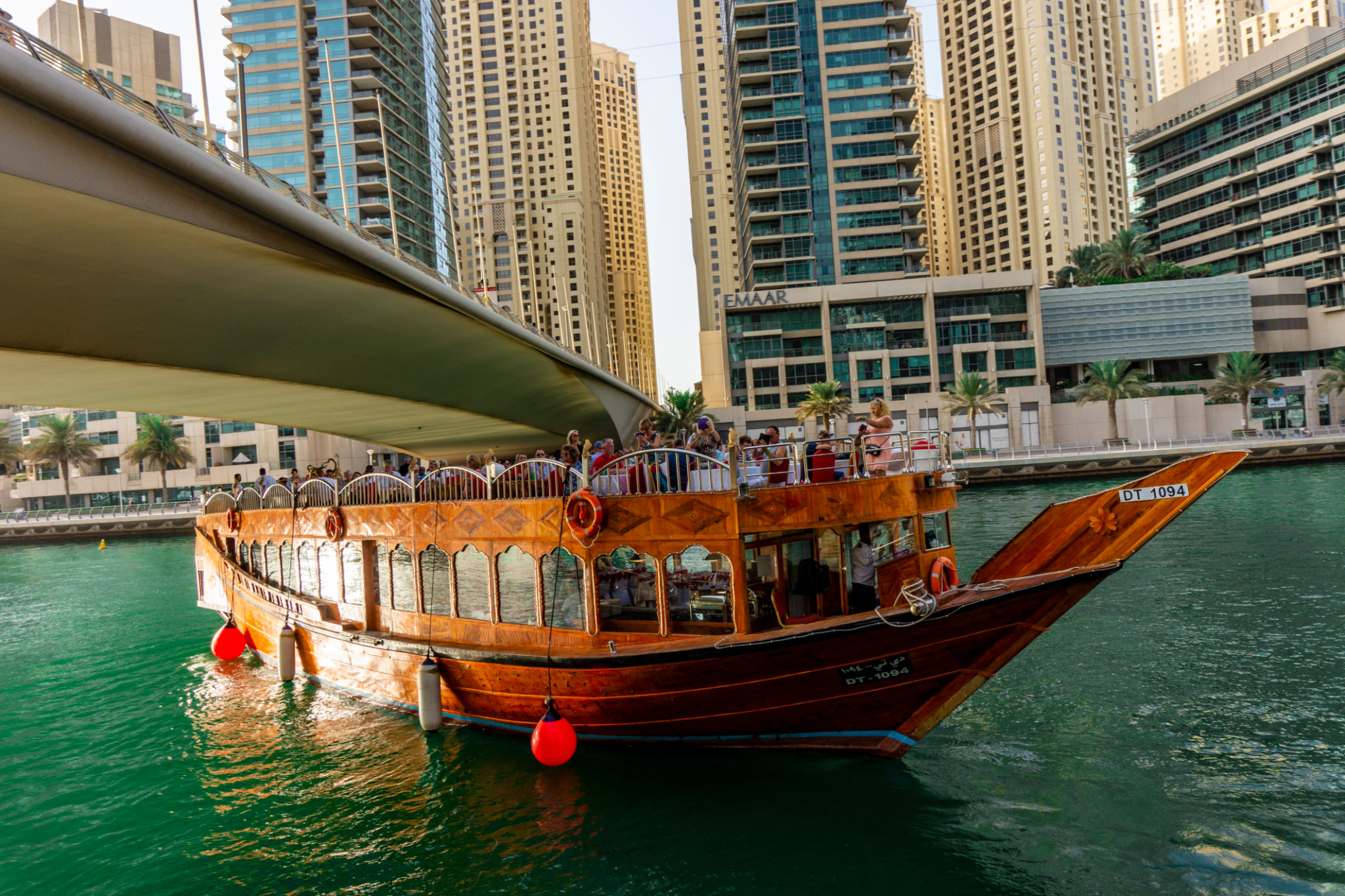 Famous traditional wooden old dhow cruise tour in the marina with tourist on the board and modern skyscrapers Famous traditional wooden old dhow cruise tour in the marina with tourist on the board and modern skyscrapers