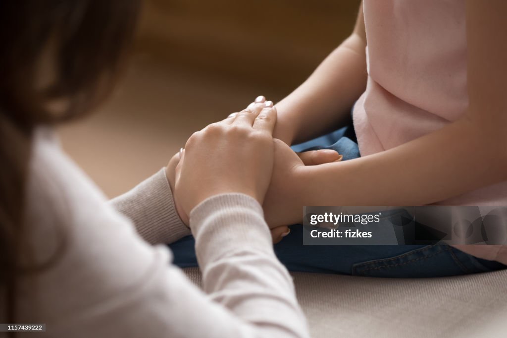 De cerca de las manos de la madre cubre las manos de la hija pequeña