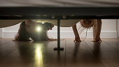 Mother and daughter shine a flashlight looking under the bed