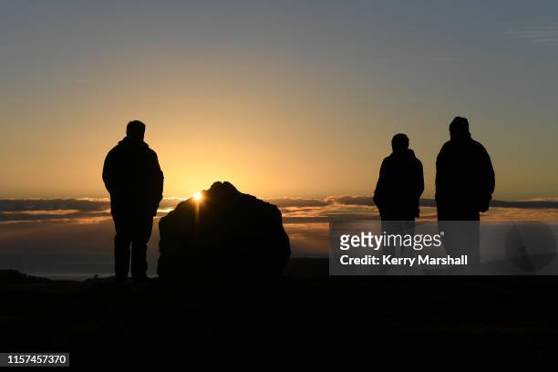 People involved in the construction and placement of stones wait for the sunrise at the Hakikino Conservation Reserve on June 22, 2019 in Waimarama,...