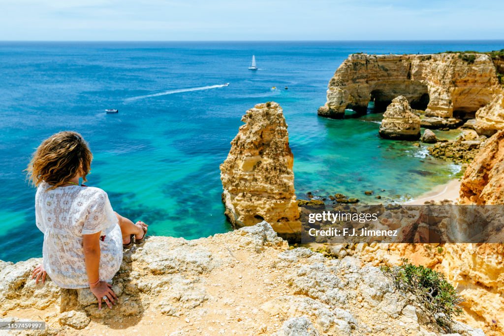 Woman on the cliffs looking towards at Praia da Marinha