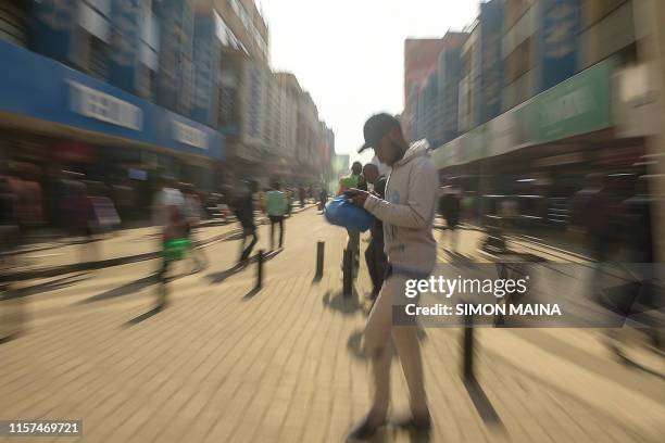 Man using his mobile phone walks along a street in down town Nairobi on July 24, 2019.