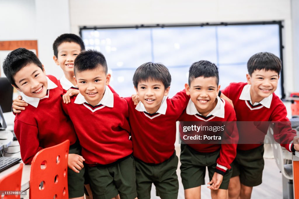 Happy schoolboys with arms around in classroom