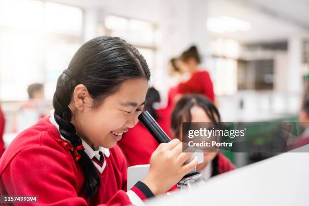 girl examining through microscope in school - middle childhood stock pictures, royalty-free photos & images