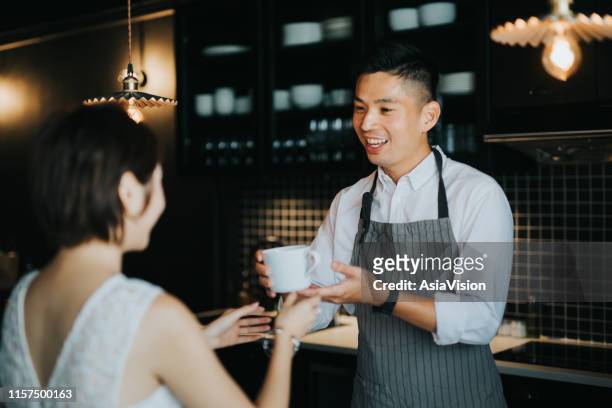de jonge aziatische barista overhandigt een koffie aan vrouwelijke klant over de café bar in het café - two executive man coffee shop stockfoto's en -beelden