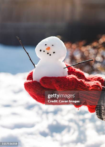 close up of hands in red wool mittens holding a small snowman. - red glove stock-fotos und bilder