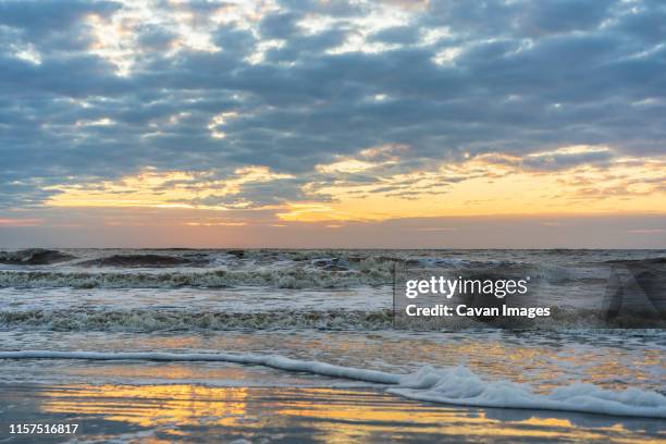 ocean waves rush toward sandy beach reflecting glowing sky at sunrise - jekyll island stockfoto's en -beelden