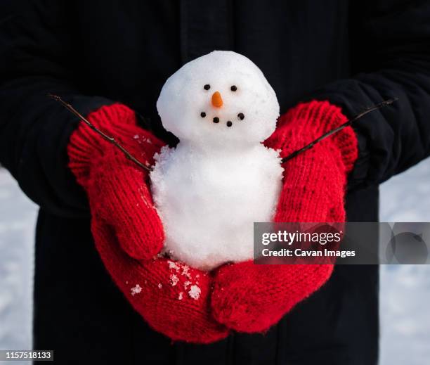 close up of hands in red wool mittens holding a small snowman. - red glove foto e immagini stock